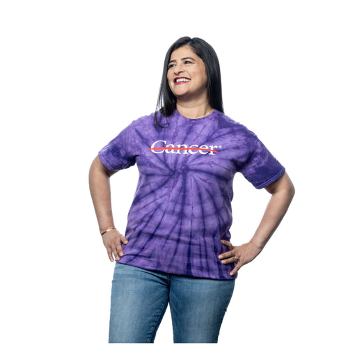 MD Anderson employee wearing a purple tie-dye shirt featuring the white cancer strikethrough logo on the chest and the white MD Anderson logo on the sleeve.