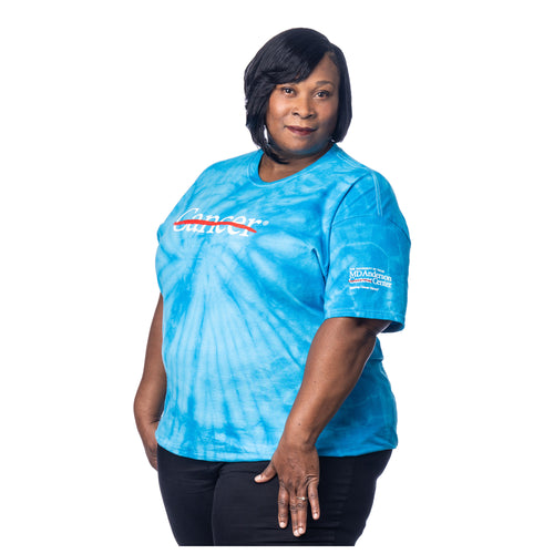 MD Anderson employee wearing a turquoise Tie-Dye shirt featuring the white cancer strikethrough logo on the chest and the full white MD Anderson logo on the sleeve.