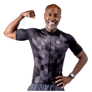 MD Anderson employee wearing a black cycling jersey with a gray grid pattern featuring the white MD Anderson logo on the upper right chest area and the white GIORDADA logo on the upper left chest area.