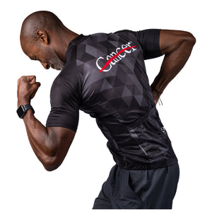 MD Anderson employee modeling the back of black cycling jersey with a gray grid pattern featuring the white cancer strikethrough logo on the top and the GIORDANA logo on the bottom.