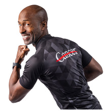 MD Anderson employee modeling the back of a black cycling jersey with a gray grid pattern featuring the white cancer strikethrough logo on the top and the GIORDANA logo on the bottom.