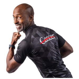 MD Anderson employee modeling the back of a black cycling jersey with a gray grid pattern featuring the white cancer strikethrough logo on the top and the GIORDANA logo on the bottom.