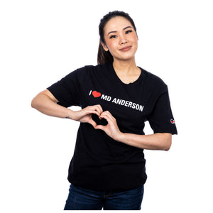 MD Anderson employee wearing a black shirt featuring the phrase "I heart MD Anderson" on the chest area and the white cancer strikethrough logo on the sleeve.