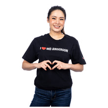 MD Anderson employee wearing a black shirt featuring the phrase "I heart MD Anderson" on the chest area and the white cancer strikethrough logo on the sleeve.