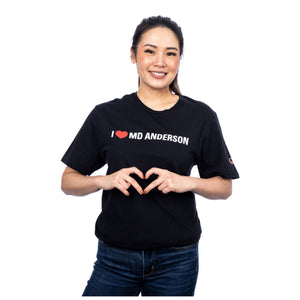 MD Anderson employee wearing a black shirt featuring the phrase "I heart MD Anderson" on the chest area and the white cancer strikethrough logo on the sleeve.