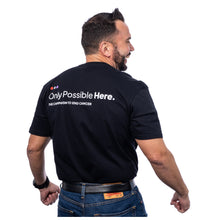 MD Anderson employee showing the back of black t-shirt featuring the tagline in white "Only Possible Here, the campaign to end cancer."