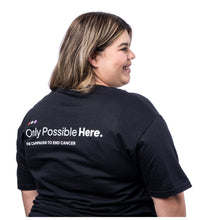 MD Anderson employee showing the back of black t-shirt featuring the tagline in white "Only Possible Here, the campaign to end cancer."