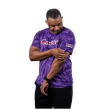 MD Anderson employee wearing a purple tie-dye short-sleeve t-shirt with the white Cancer strikethrough logo across the chest and the UT MD Anderson logo on the sleeve.