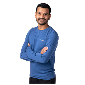 MD Anderson employee wearing a blue long sleeve shirt featuring the white cancer strikethrough logo on the upper left chest area.