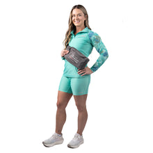 MD Anderson employee wearing the matching turquoise 1/4 zip and shorts which both feature the white cancer strikethrough logo, and also sporting a gray belt bag featuring the full white MD Anderson logo on it.