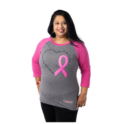 MD Anderson employee wearing a gray raglan tee with pink quarter length sleeves featuring a pink ribbon for breast cancer awareness month and a heart. Also featuring the white cancer strikethrough logo at the bottom hem.