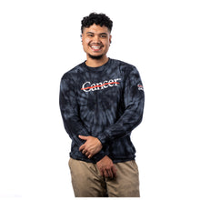 MD Anderson employee wearing a black tie-dye long-sleeve shirt featuring the white Cancer strikethrough logo across the chest and the UT MD Anderson logo on the sleeve.