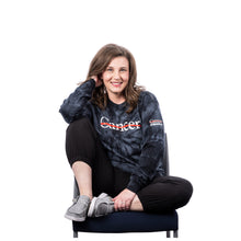 MD Anderson employee wearing a black tie-dye long-sleeve shirt featuring the white Cancer strikethrough logo across the chest and the UT MD Anderson logo on the sleeve.