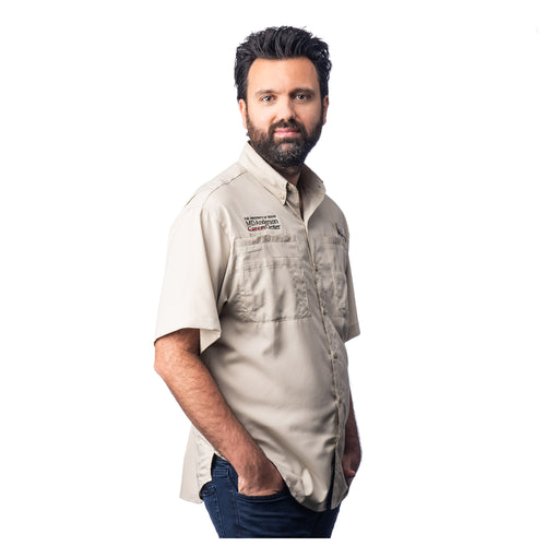 MD Anderson employee wearing a short sleeve tan Columbia button-up shirt with two chest pockets, featuring the black MD Anderson logo on one side and the Columbia logo on the other side.