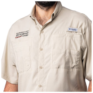 Closeup of MD Anderson employee wearing a short sleeve tan Columbia button-up shirt with two chest pockets, featuring the black MD Anderson logo on one side and the Columbia logo on the other side.