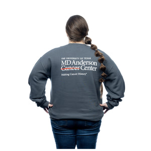 MD Anderson employee wearing a gray crewneck featuring the white cancer strikethrough logo on the chest area and the back featuring the full MD Anderson logo.