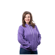 MD Anderson employee wearing a heather purple hooded sweatshirt featuring the white Cancer strikethrough logo on the left chest, a kangaroo pouch pocket, and "Making Cancer History" printed down the right sleeve.
