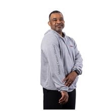 MD Anderson employee wearing an athletic heather gray hooded sweatshirt featuring the white Cancer strikethrough logo on the left chest and "Making Cancer History" printed down the right sleeve.