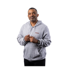 MD Anderson employee wearing an athletic heather gray hooded sweatshirt featuring the white Cancer strikethrough logo on the left chest, white hood drawcords, and a kangaroo pouch pocket.