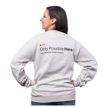 MD Anderson employee showing the back of heather oatmeal crewneck featuring the black tagline "Only Possible Here, the campaign to end cancer."
