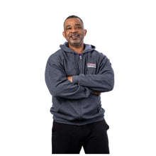 MD Anderson employee wearing a dark heather gray long-sleeve full-zip fleece hoodie with arms crossed, featuring the white Cancer strikethrough logo on the left chest.