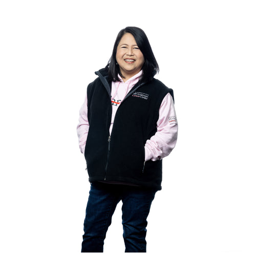 MD Anderson employee wearing a black fleece zippered vest with the white MD Anderson logo embroidered on the chest area, and also a pink hooded cancer strikethrough hoodie.