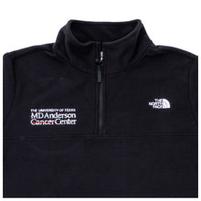 Closer-up image of black North Face jacket featuring a quarter-zip, the white MD Anderson logo on the right and the North Face logo on the left side of the chest.