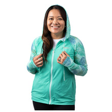 MD Anderson employee wearing a turquoise hoodie featuring the white cancer strikethrough logo on the upper left chest area with a tropical leaves print on the sleeves.