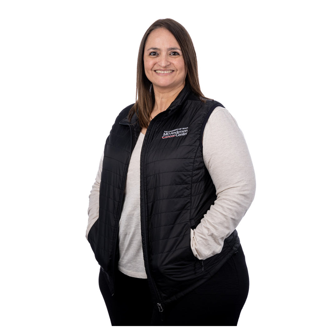 MD Anderson employee wearing a black puffy zippered vest with front pockets featuring the full white MD Anderson logo on the top left chest area.