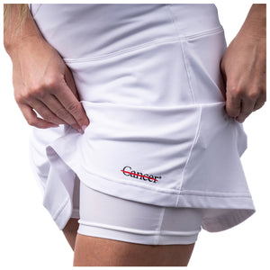 White skort featuring the black cancer strikethrough logo on the bottom seam showing the shorts underneath.