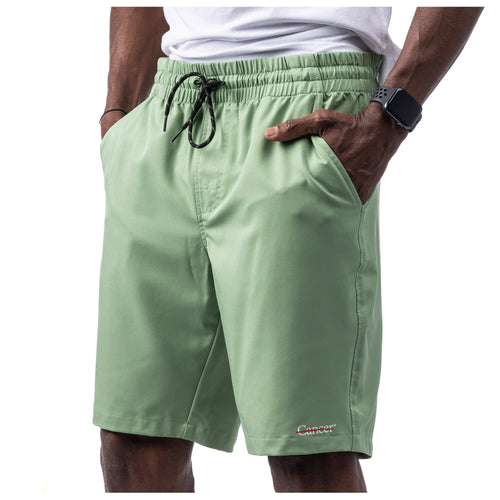 MD Anderson employee wearing basil green shorts with side pockets featuring the white cancer strikethrough logo on the bottom left seam.