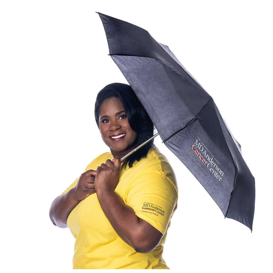 MD Anderson employee holding a black umbrella featuring the full white MD Anderson logo, and wearing the daisy cancer strikethrough shirt featuring the full black MD Anderson logo on the sleeve.