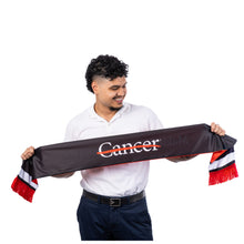 MD Anderson employee holding up the black side of a knit soccer scarf featuring the white Cancer strikethrough logo on the front and white-and-red stripe trim with fringe ends.