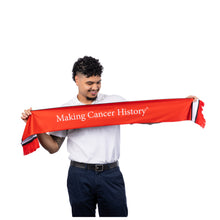 MD Anderson employee holding up the red side of a knit soccer scarf featuring the white "Making Cancer History" tagline across the front and white-and-black stripe trim with fringe ends.