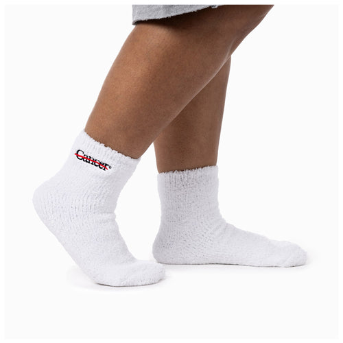 MD Anderson employee wearing white fuzzy socks with the black cancer strikethrough logo on the side and non-slip grip bottoms.