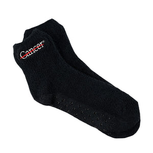 Black fuzzy socks with the white cancer strikethrough logo on the side and non-slip grip bottoms.